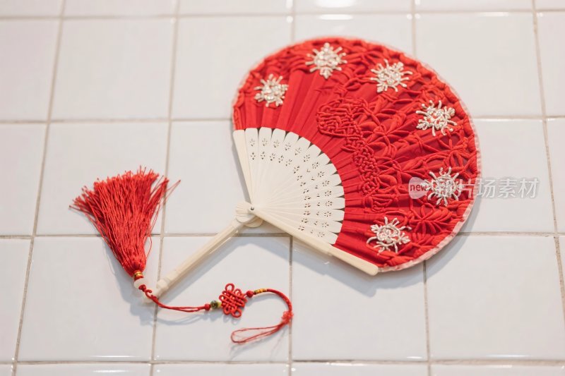 红色绣花折扇置于白瓷砖上
