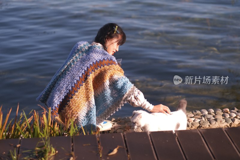 温暖阳光下在湖边和小猫玩耍的温柔女子肖像