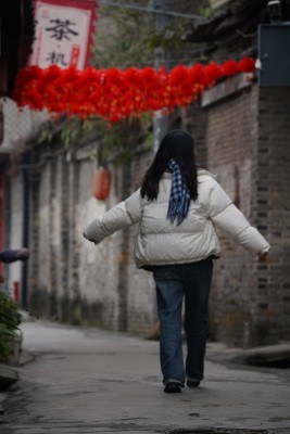 穿冬装女子在挂有红灯笼的古镇小巷行走