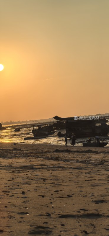 夕阳下的海滩边有船只和人影