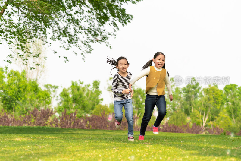 夏天两名牵手在公园草坪上奔跑中国女孩