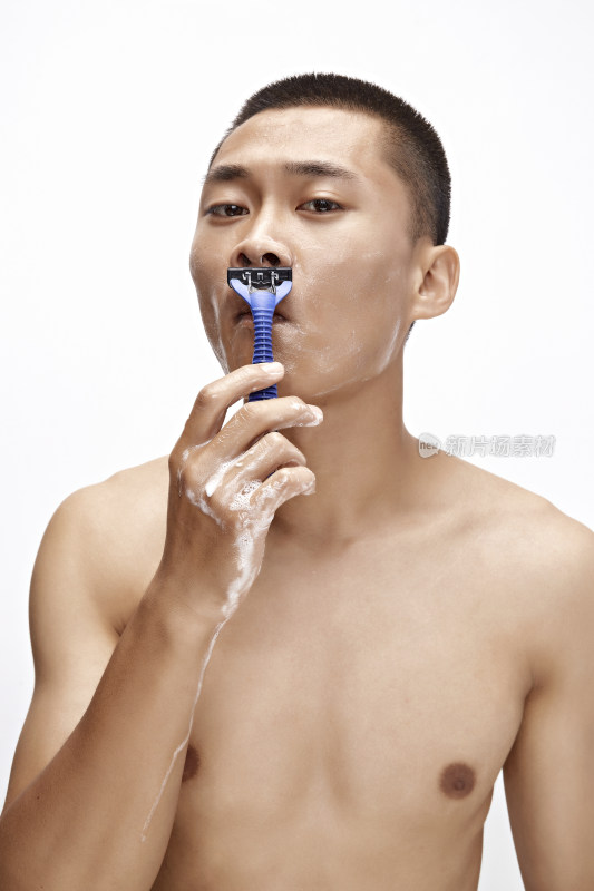 白色背景下手持剃须刀在刮胡子的亚洲男性