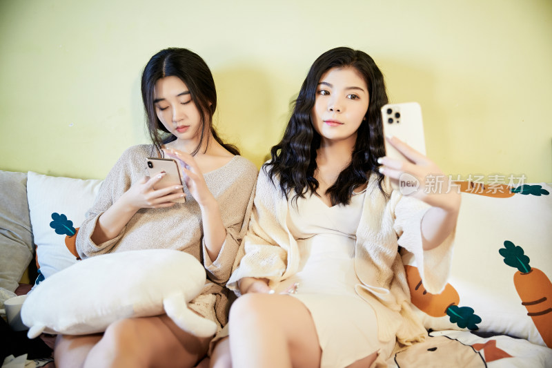坐在床上玩手机的俩位美女