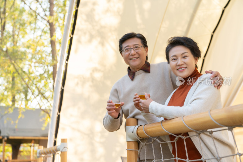 中老年夫妻搂着肩膀在露营地喝茶聊天
