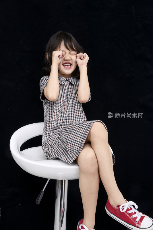 黑色背景里坐在凳子上的可爱的亚洲小女孩（儿童）