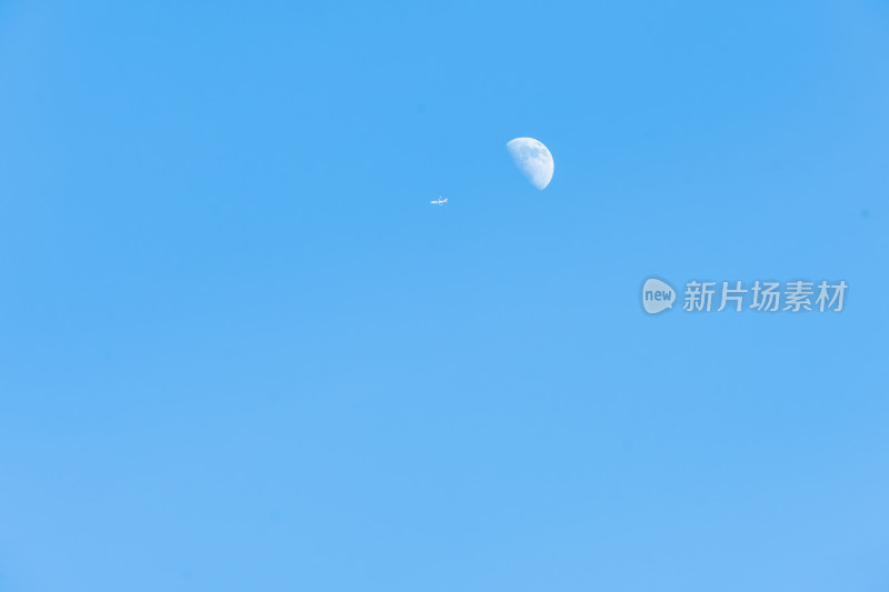 蓝色天空中月亮下一架飞行的客机