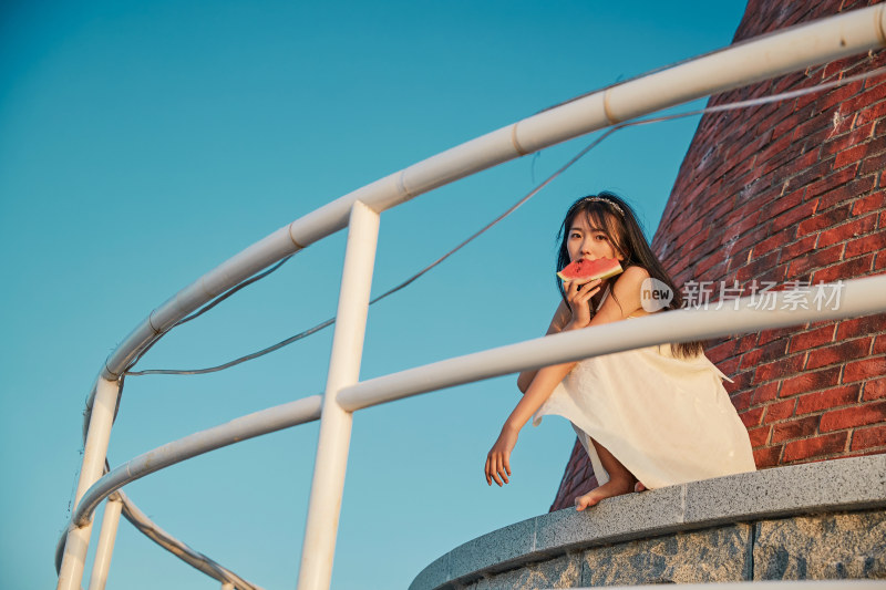 盛夏夕阳湖边码头灯塔上吃西瓜的少女
