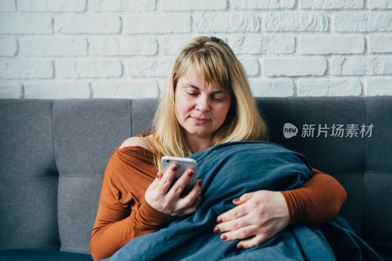 女性沙发上裹毛毯玩手机