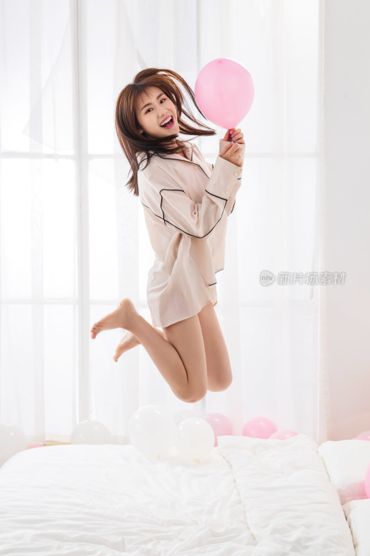 年轻女人拿着气球在床上跳跃玩耍