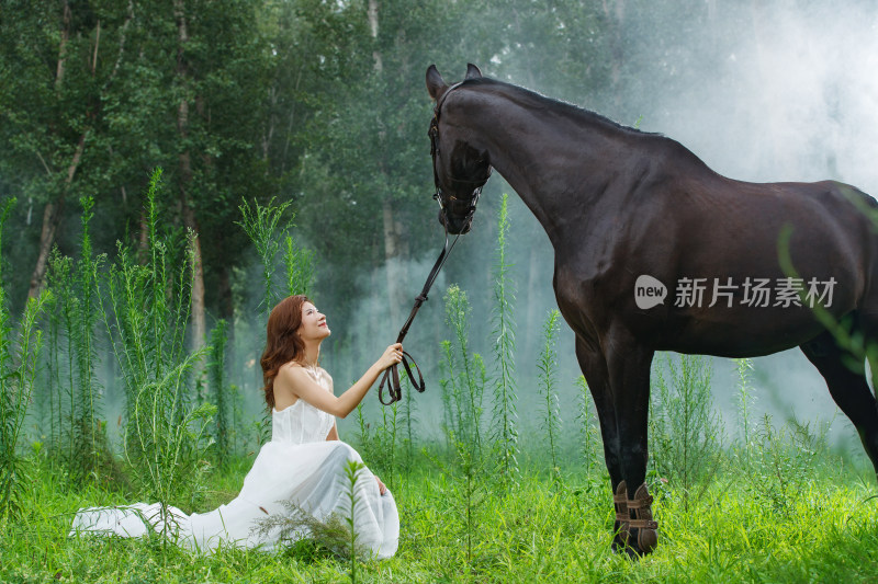 草地上穿婚纱的漂亮年轻女人和马