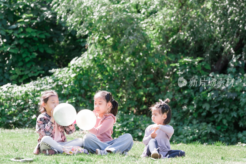 秋天午后三个坐在草坪上玩气球的女孩