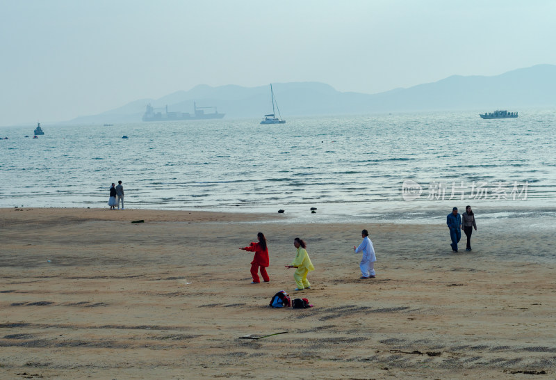 青岛海水浴场沙滩上，三个练太极的人