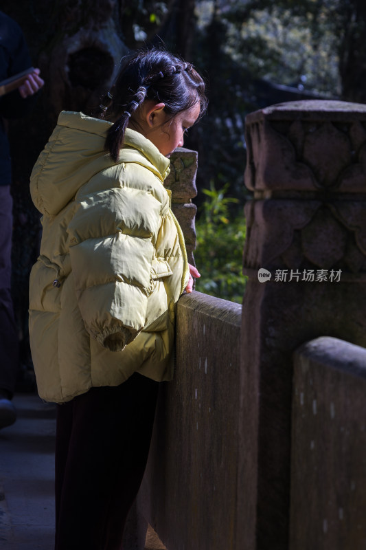 穿黄色棉服的小女孩靠在石栏杆上