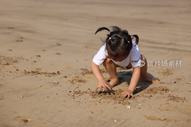 小女孩在沙滩上专注玩沙的可爱场景