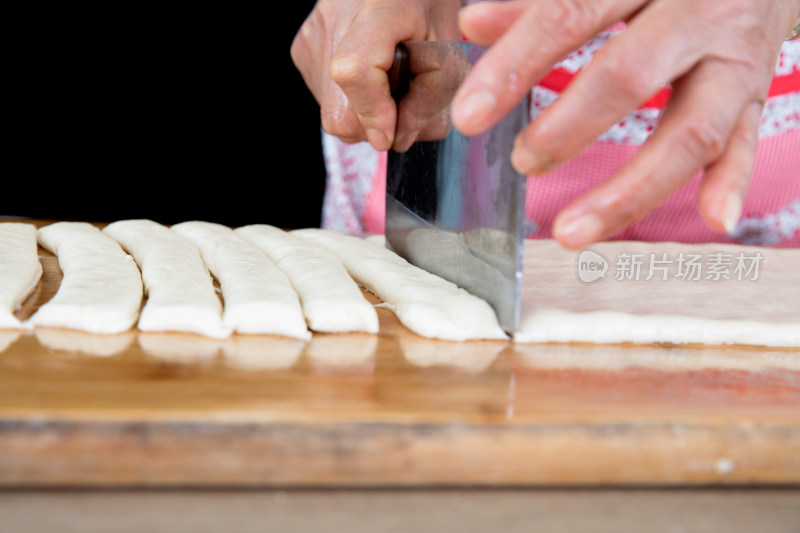 厨师用刀把饼状的油条面切成长条状