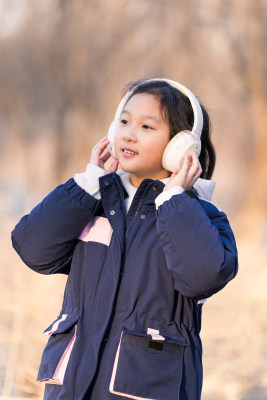 冬日暖阳在公园树林中带耳机欣赏音乐的女孩