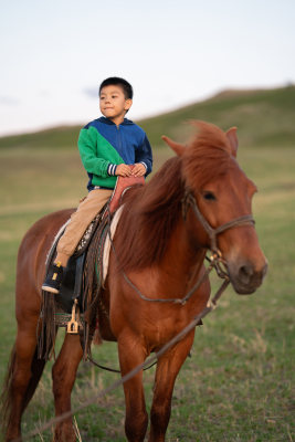 一个小男孩在落日的草原上骑马
