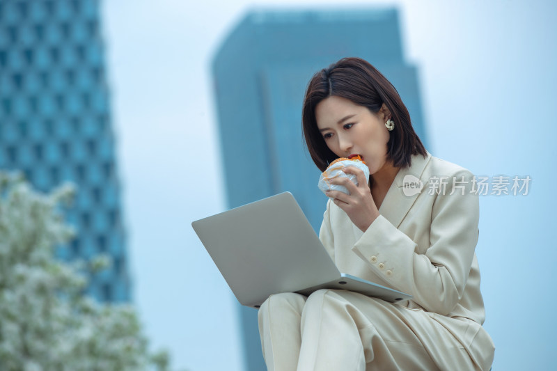 商务女士在户外边吃饭边用电脑