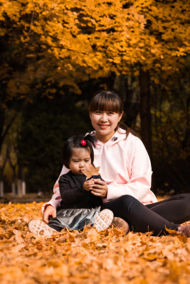 深秋坐在公园落满黄叶的草地上的中国母女