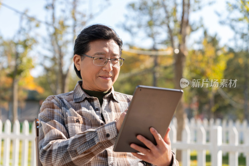 一个老年男人坐在露营院子里看平板电脑