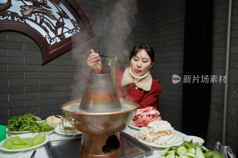 在饭店吃传统铜锅涮肉的亚洲少女