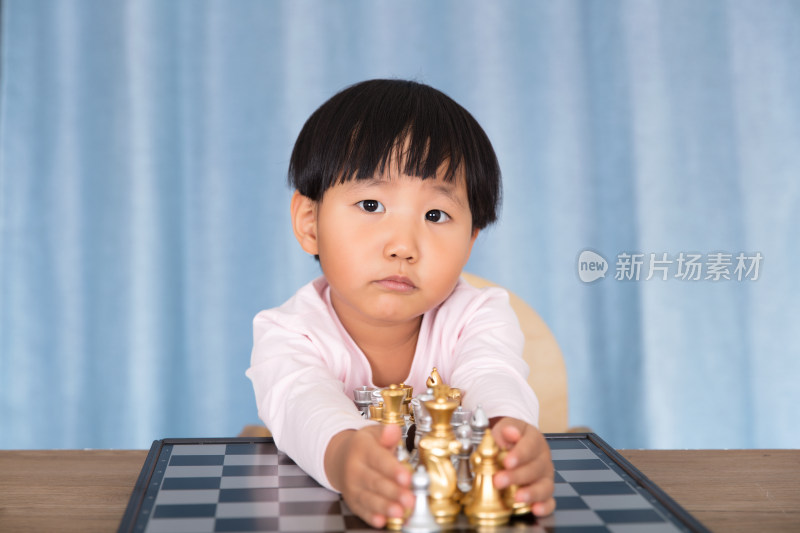 中国小孩子双手抱着国际象棋棋盘上的棋子