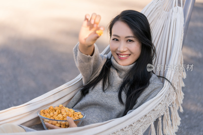 年轻女子坐在吊床上吃爆米花