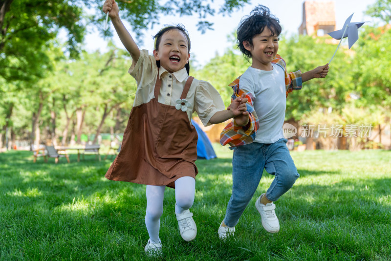 两个小孩子在草地上举着风车开心奔跑