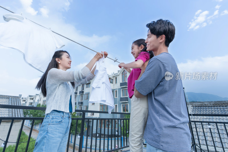 年轻爸爸抱着女儿和妈妈一起晾衣服