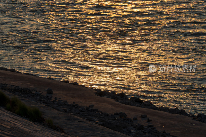 夕阳下波光粼粼的水面与岸边岩石景象