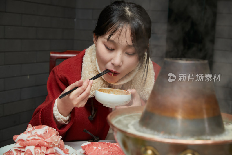 在饭店吃传统铜锅涮肉的亚洲少女