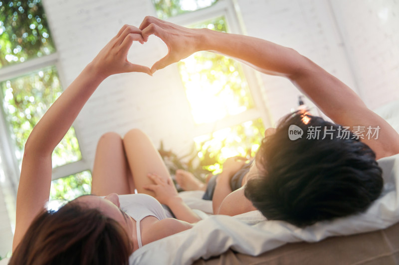 幸福的年轻伴侣躺在床上做心形手势