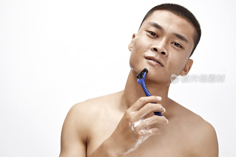 白色背景下手持剃须刀在刮胡子的亚洲男性