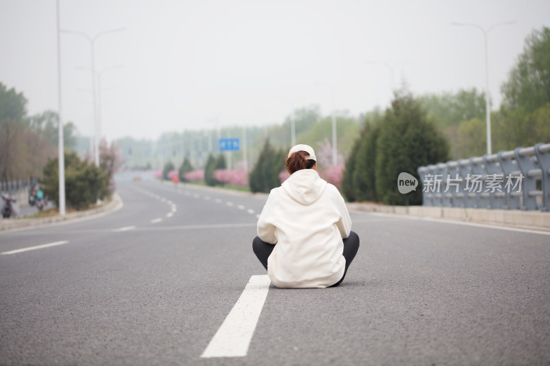 年轻的女性坐在马路中间拍摄后背照