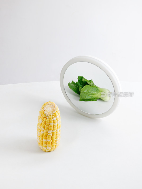 桌面上摆放着一根玉米和镜子中的一颗青菜