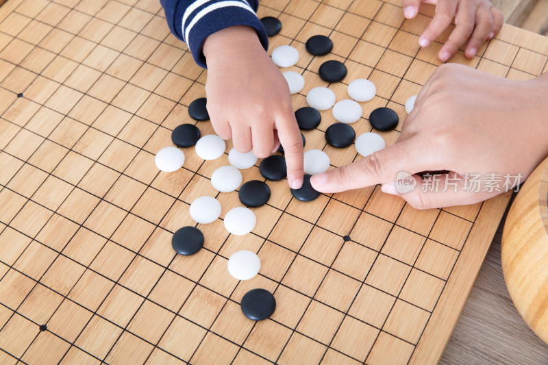 一只大人的手指导着小孩的手下围棋