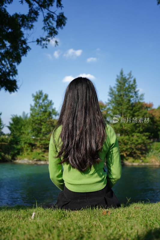 背对着天空坐在湖边的女人的后视图