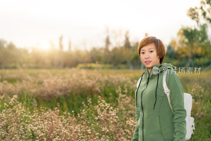 年轻的中国籍女性站在公园的花丛前