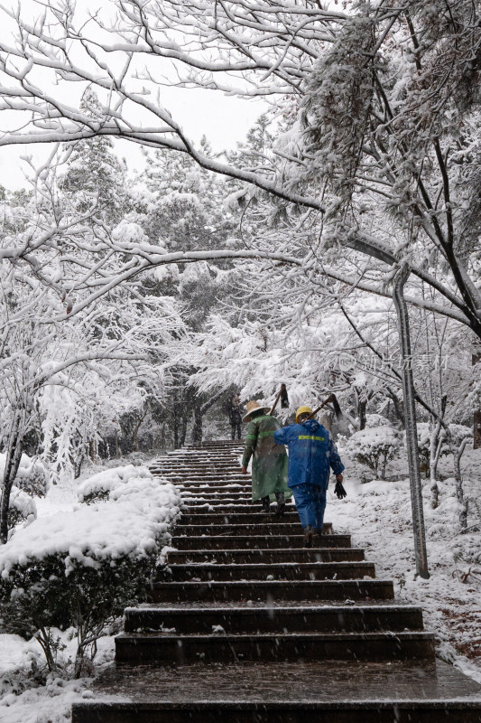 雪中两名工人行走在积雪的台阶上