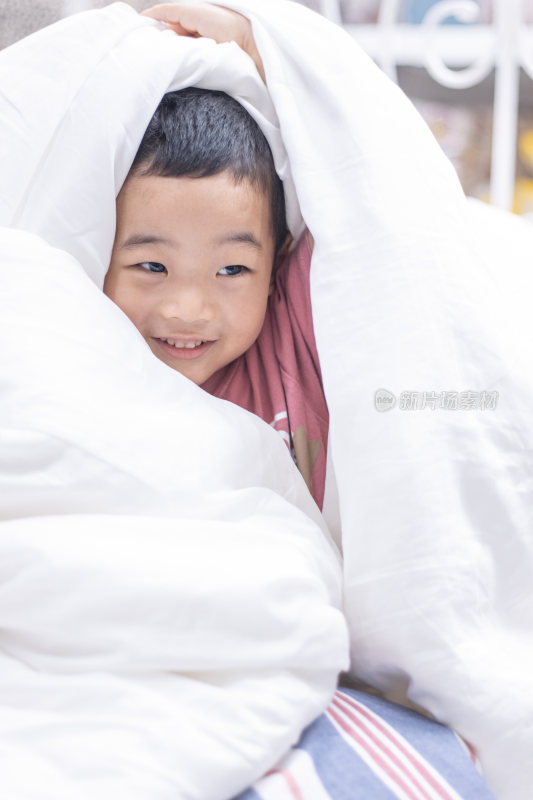 一个小男孩盖着被子在床上玩耍