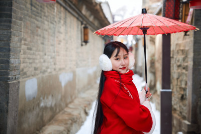 雪后在老城古巷穿着喜庆服饰的亚洲少女