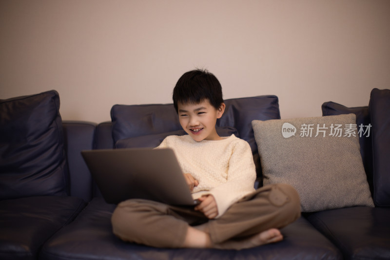 一个帅气的中国小男孩坐在沙发上看电脑