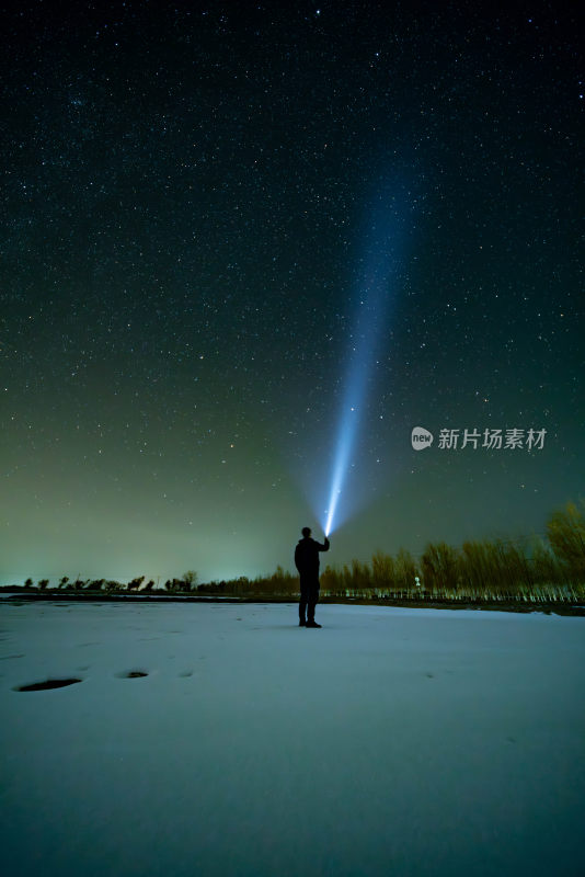 雪地上男子用手电筒照射夜空的场景