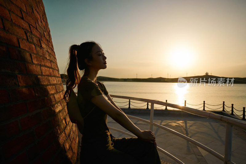 盛夏夕阳晚霞湖边码头灯塔上的少女