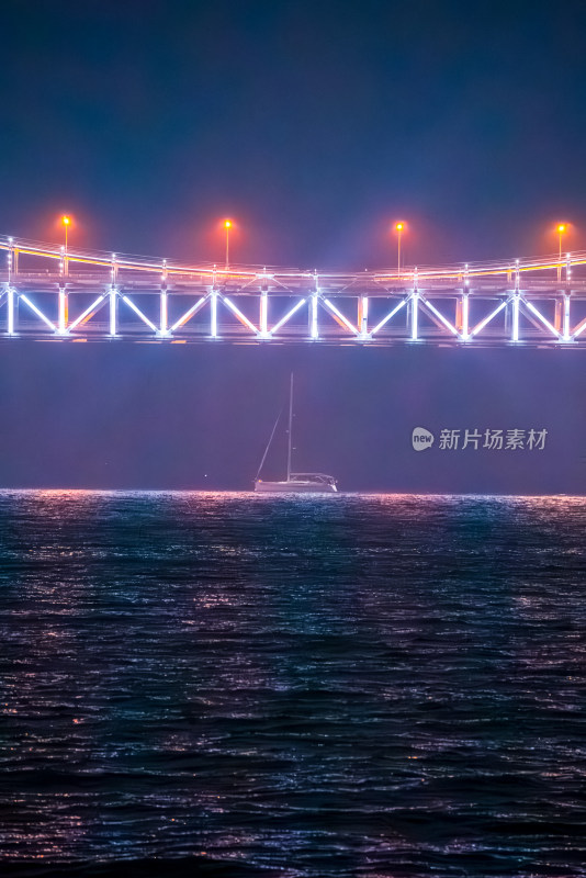 夜景中灯火辉煌的跨海大桥和海中帆船