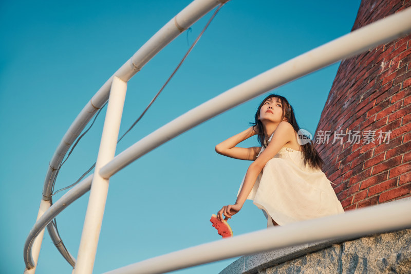 盛夏夕阳湖边码头灯塔上吃西瓜的少女