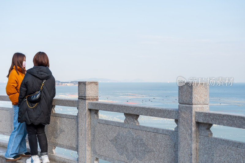 两位女性海边栏杆旁眺望海景