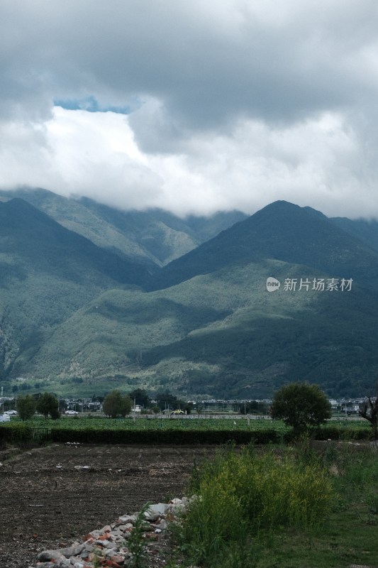 阴云下的青山远景及山脚下的土地