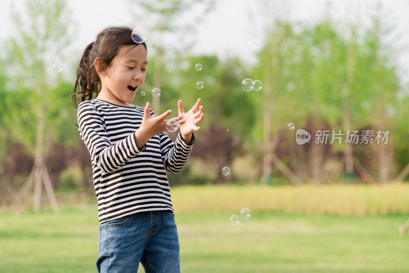 在草坪上玩吹泡泡游戏的女孩