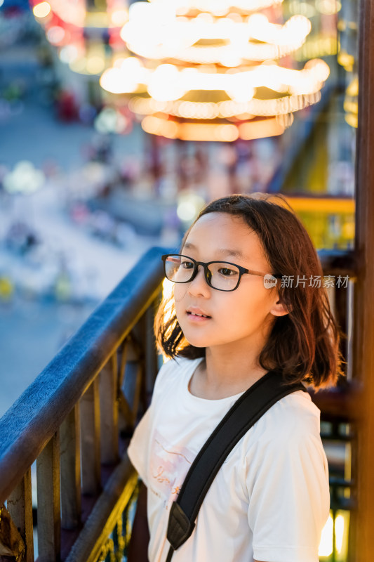 戴眼镜女孩倚栏杆望城市夜景